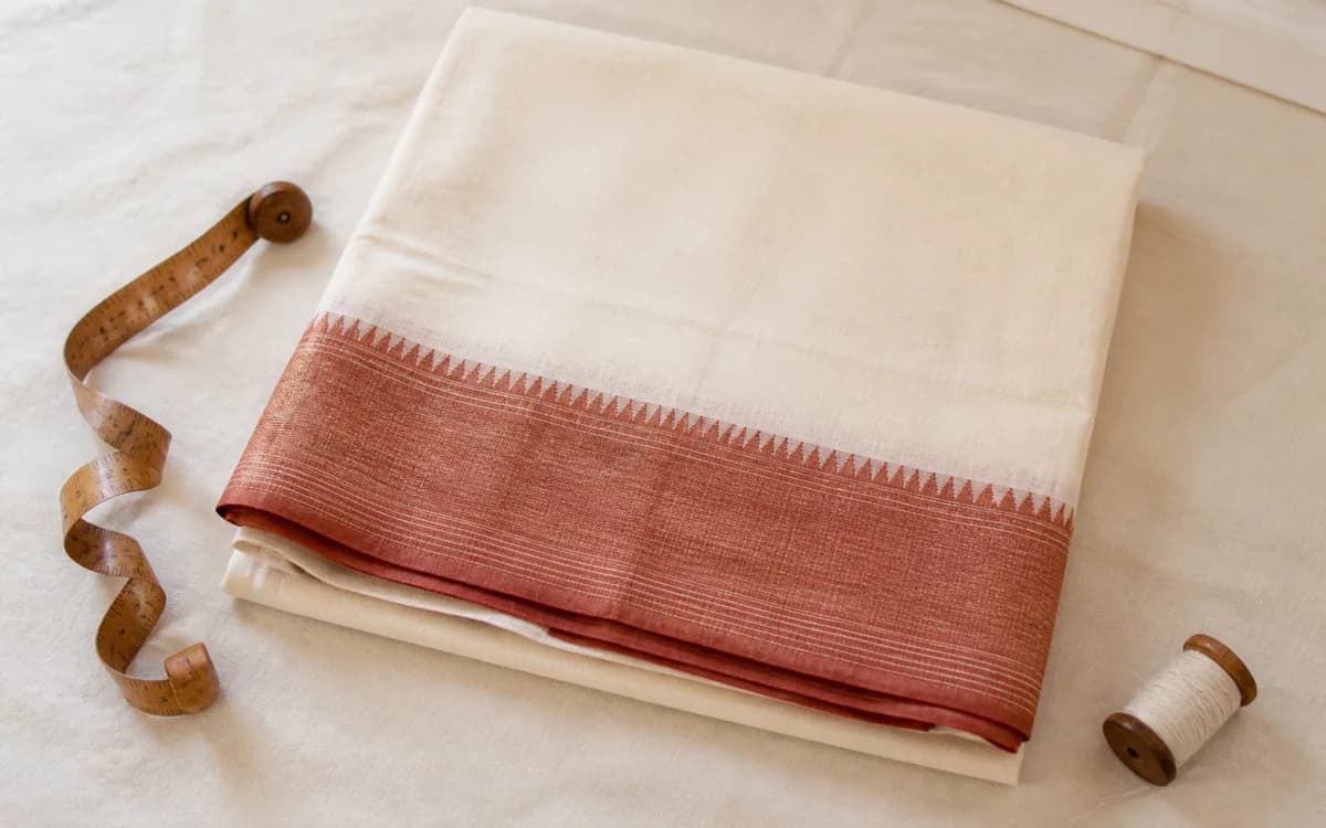 Editorial still life of an ivory saree with a muted terracotta woven border, representing sarees sourcing in Surat, Gujarat